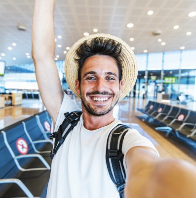 Happy tourist man taking a selfie portrait with mobile smart phone at airport - Airplane passenger waiting for flight - Travel without restrictions concept